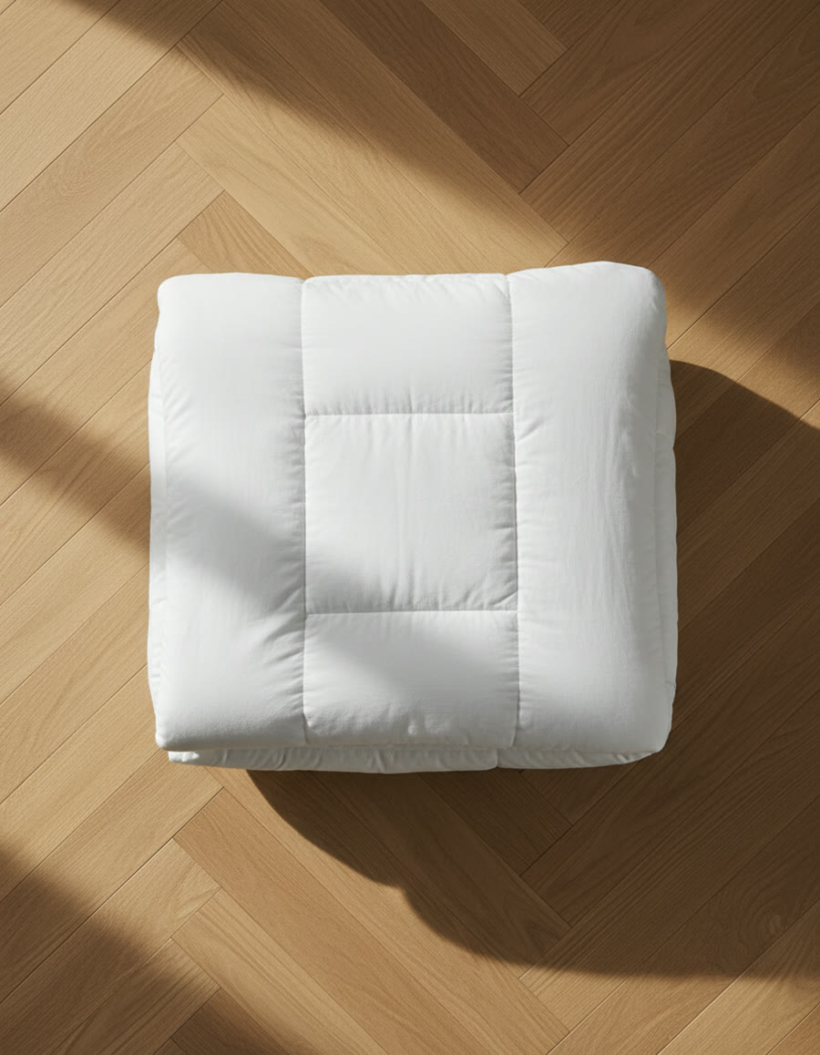 A white duvet folded into a neat quarter-fold on a light oak herringbone floor.